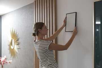 Woman arranging picture frames on wall in new house, diy home improvement concept	