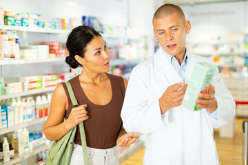 Male pharmacist consulting oriental woman about treatment in drugstore.