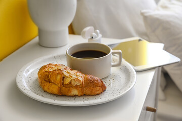 Plate with tasty croissant and cup of aromatic coffee on table in bedroom, closeup