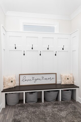 A cozy mudroom with hooks on board and batten walls, a wooden bench seat, and a rug on a tiled...