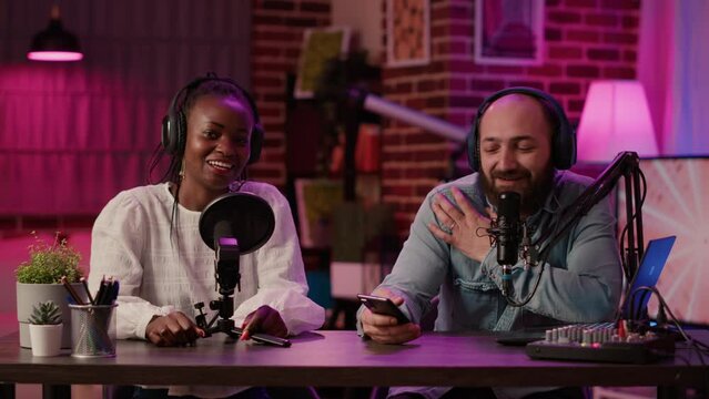 Diverse team of online radio hosts recording podcast review for smartphone streaming audio with digital mixer. Content creator and african american influencer broadcasting live product presentation.