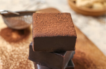 Stack of tasty bird's milk candies with cocoa powder on table, closeup