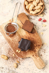 Wooden board with tasty bird's milk candies, cocoa powder and nuts on light background