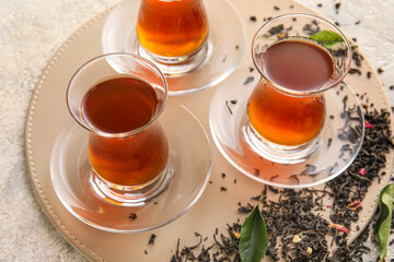 Glass cups of black tea and dried leaves on light background, closeup