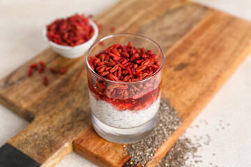 Wooden board with glass of tasty chia seed pudding and barberry on light table, closeup