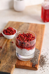 Wooden board with glass of tasty chia seed pudding and barberry on light table, closeup