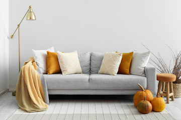 Autumn interior of living room with grey sofa, lamp and pumpkins