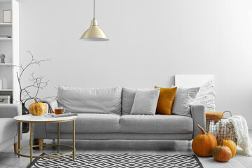 Autumn interior of living room with grey sofa, table and pumpkins