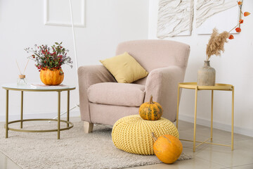 Interior of light living room with autumn flowers in pumpkin and armchair