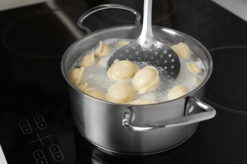 Cooking dumplings in saucepan with boiling water on cooktop, closeup