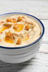 Bowl of tasty hummus with chickpeas and paprika on white wooden table, closeup