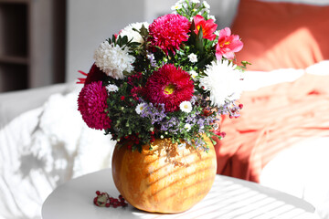 Pumpkin with autumn flowers on table in light bedroom, closeup