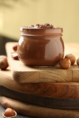 Glass jar with tasty chocolate hazelnut spread and nuts on wooden board