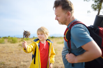 Naklejka premium Cute schoolchild and his mature father hiking together and exploring nature. Little boy and his dad spend quality family time on summer vacation. Father's Day.