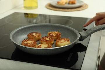 Woman frying delicious cottage cheese pancakes in kitchen, closeup