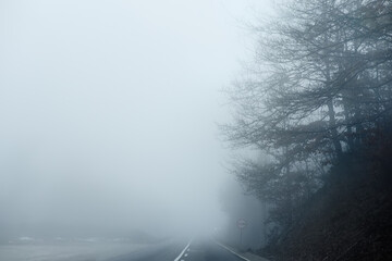 Thick fog on the highway in Europe on a winter day. The danger of driving of vehicles on roads in bad foggy weather. Insurance of safety of drivers and cars.