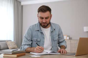 Young man taking notes during online webinar at table indoors