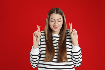 Woman with crossed fingers on red background. Superstition concept