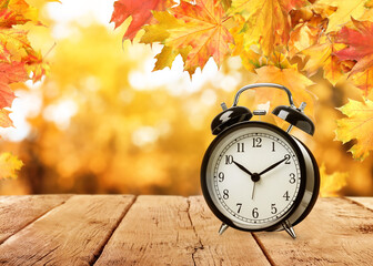 Alarm clock on wooden table and beautiful autumn leaves against blurred background, space for text....