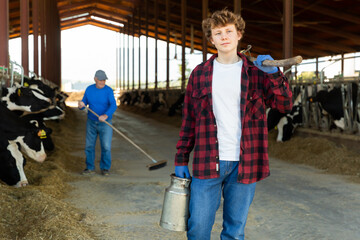 Fototapeta premium Young farmer diligently cleans the barn and feeds the cows with hay