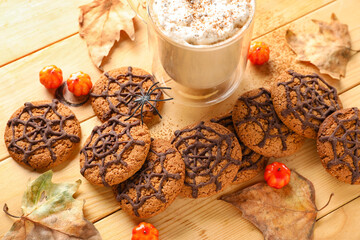 Halloween spiderweb cookies with glass of cocoa, candies and fallen leaves on wooden background