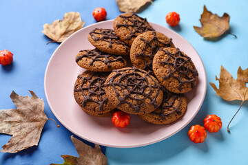 Plate with Halloween spiderweb cookies, fallen leaves and candies on blue background
