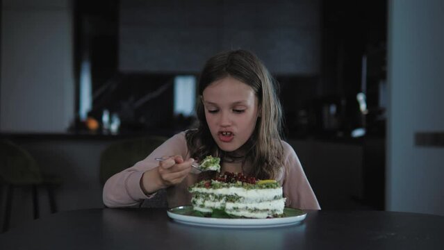 Hungry funny kid female eating birthday cake alone, having fun, dancing, making funny face expressions. Kid child girl  enjoying delicious homemade cake, sitting alone in the kitchen. Lonely birthday