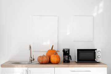 Kitchen counters with Halloween pumpkins, coffee maker and microwave oven near light wall