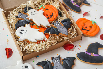 Cardboard box with Halloween cookies, sprinkles and leaves on white wooden background