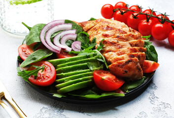 Fresh vegetable salad with grilled chicken fillet, spinach, tomatoes, avocado and red onion with olive oil on white background. Healthy, detox, ketogenic diet food. Top view