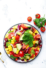 Mexican spicy salad with corn, red beans, avocado, jalapeno, tomatoes, onion and cilantro. White stone table background, top view