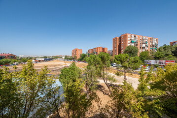 Views of the trees of an urban park and residential buildings surrounded by leafy trees in the background