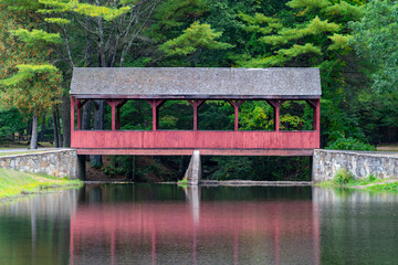 Red covered bridge rests over a fishing pond in early Autumn 2022.