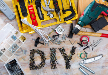 Word DIY lined with metal screws among assorted fasteners, supplies and hand tools on wooden table