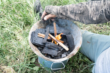 El señor está preparando el asador con las astillas de madera, el carbón y la cerilla para...