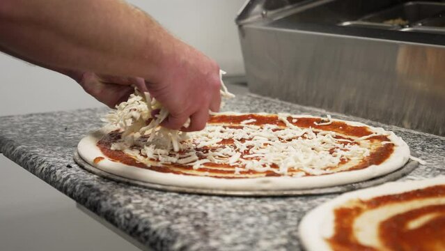 Chef sprinkles handfuls of shredded mozzarella cheese over pizza dough covered in red sauce, slow motion 4K