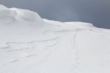 Drifting snow blowing over large white snowdrift