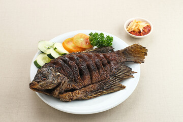 Gurame Bakar Madu, Grilled Gourami with honey and soy sauce. Served with sambal (chilli sauce), cucumber and tomatoes in white plate.   
