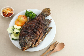 Gurame Bakar Madu, Grilled Gourami with honey and soy sauce. Served with sambal (chilli sauce), cucumber and tomatoes in white plate.   
