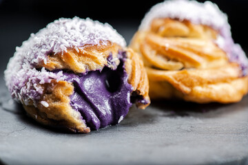 Home-made ube cream puff with purple-colored white chocolate and coconut, also known as a Profiterole.