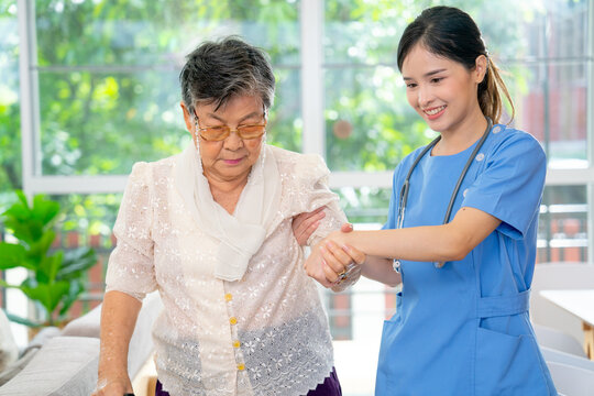 Beautiful Asian nurse or doctor support senior woman by hold arm and hands during walk in the way in clinic or hospital.