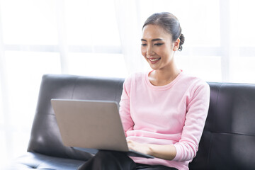 Beautiful Young Asian woman using laptop computer on sofa at home, shopping online with internet in happy mood and Relax part time concept
