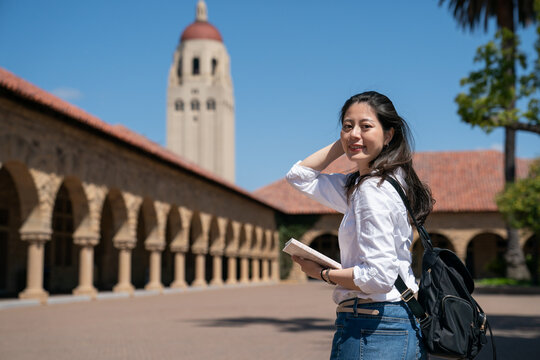 attractive asian Chinese female exchange student pushing hair back and turning to look at camera at memorial court with hoover tower in distance background on Stanford campus