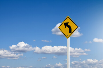 Traffic sign; left arrow curve sign on white pole by the main road with blue sky background, soft...