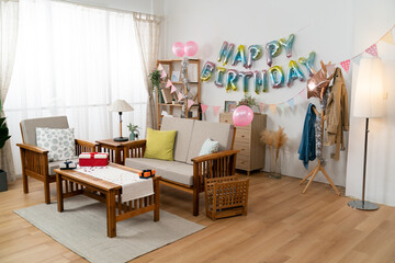 wide angle shot of a modern bright home interior with cute birthday party decoration  with birthday garland, pink balloons and gifts