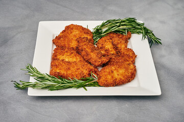 Organic breaded chicken cutlet served on a plate with rosemary garnish