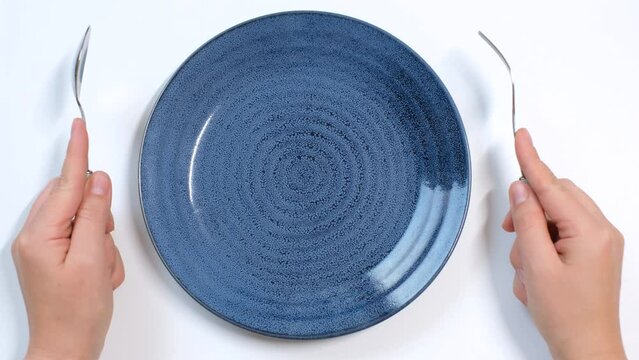 Empty plate and female hand with fork on white background close-up top view.