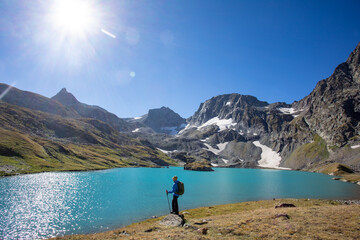Fototapeta na wymiar The girl stands against the backdrop of mountain peaks and a blue lake. Beautiful mountain landscape for vacation, travel and healthy lifestyle