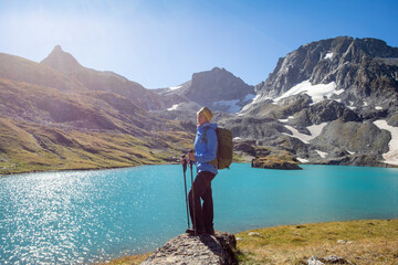 Fototapeta na wymiar The girl stands against the backdrop of mountain peaks and a blue lake. Beautiful mountain landscape for vacation, travel and healthy lifestyle