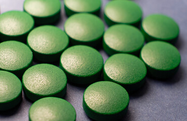 A macro shot of a green pill on a blue background. A lot of big green tablets spread over surface